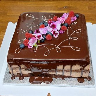 Suklaakuorrutteinen kakku kukka- ja marjakoristeilla